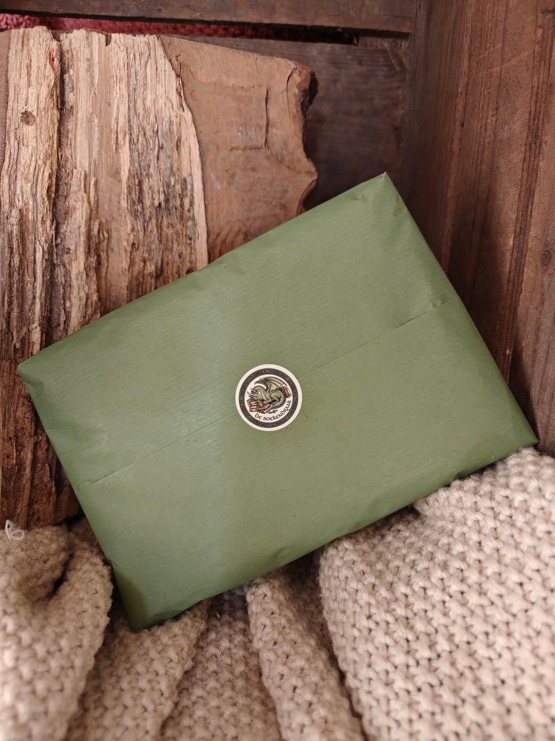 A green paper wrapped package displayed on fabric in a wood case.